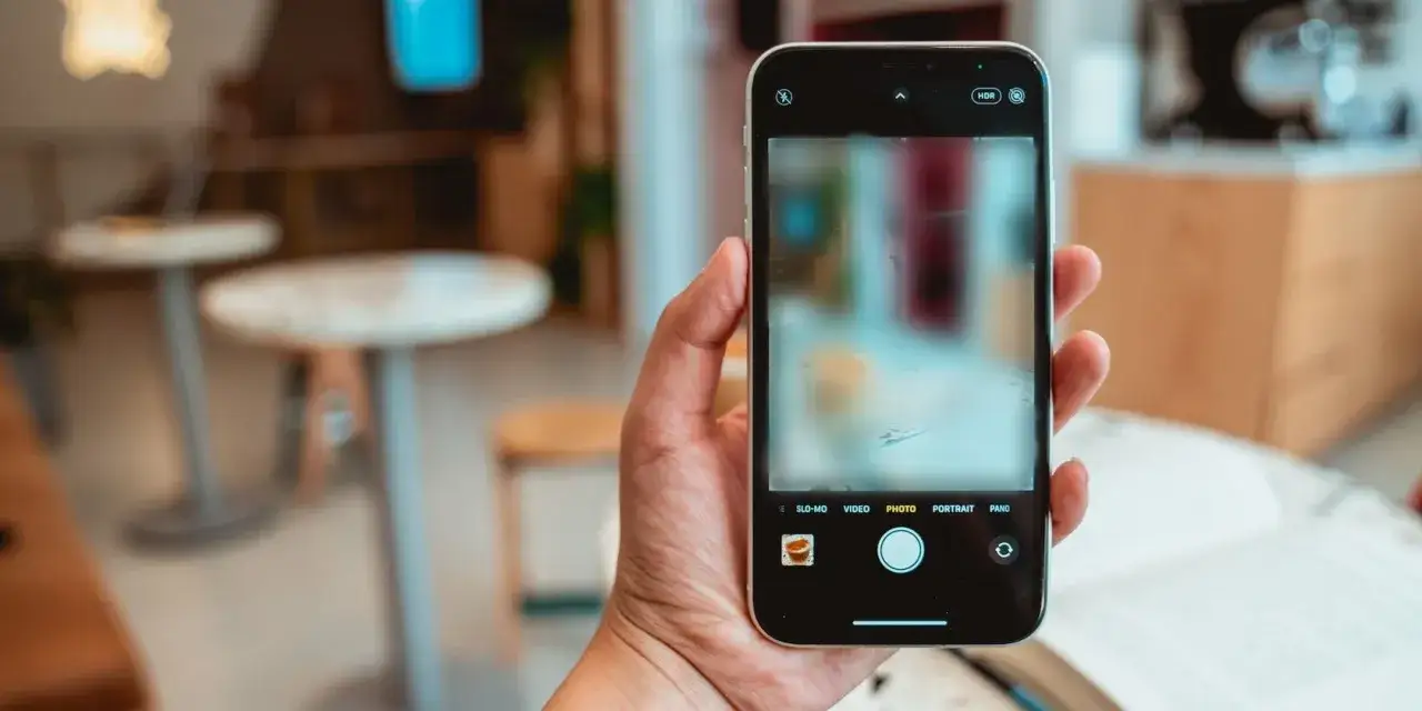 Mano che tiene uno smartphone, con l'interfaccia della fotocamera visibile. L'immagine sullo schermo è sfocata, forse perche la fotocamera interna è sfocata o per un effetto artistico.