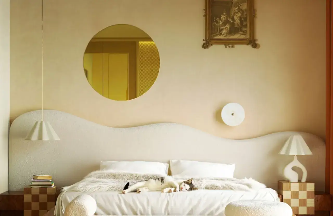 Un chat dort sur un lit douillet. La chambre beige est d&eacute;cor&eacute;e d'un miroir rond et d'un tableau. Quelle couleur assortir avec le beige ? Le dor&eacute; et le blanc cr&eacute;ent une ambiance chaleureuse.