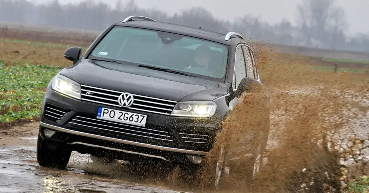 Czarny VW Touareg 3.0 TDI pokonuje błotnistą kałużę, wzbijając fontannę brudu.