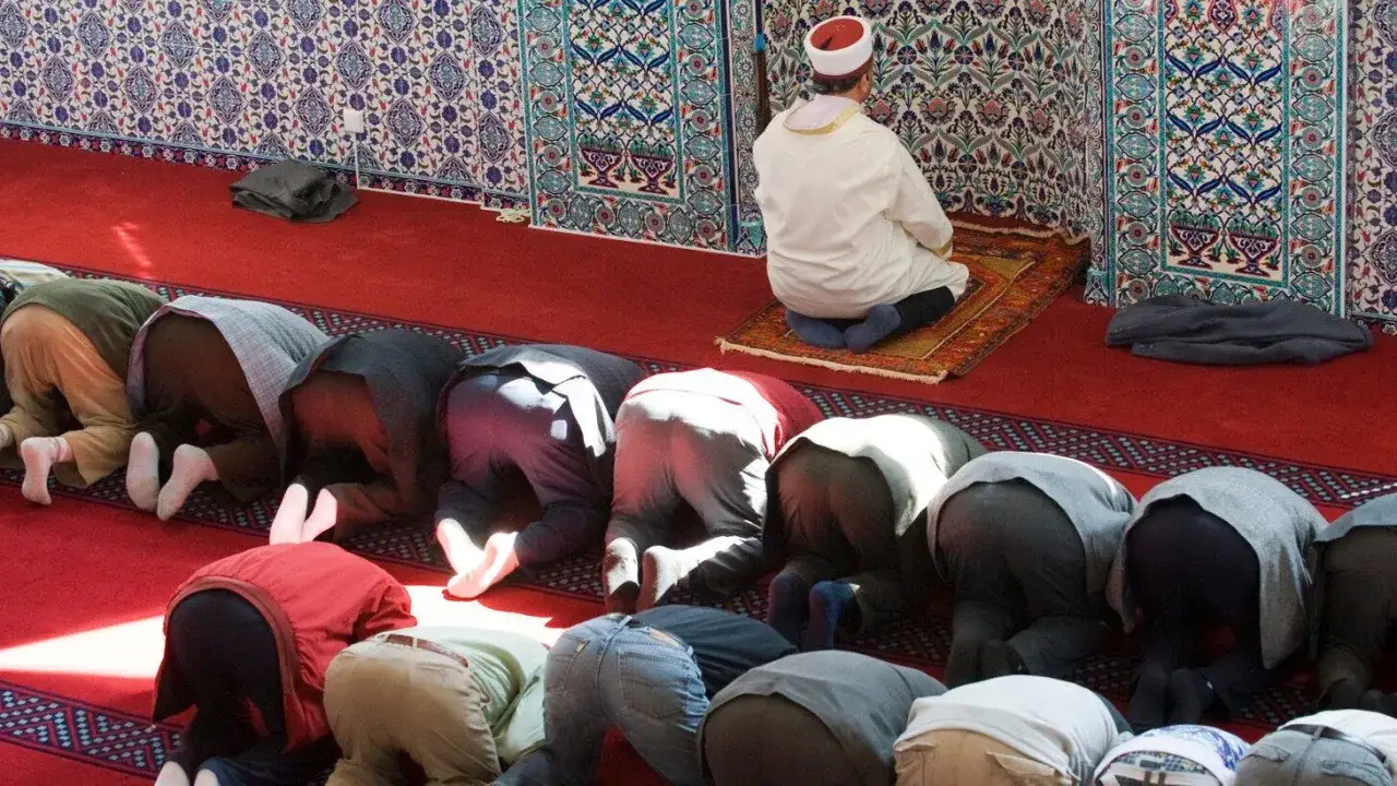 M&auml;n ber p&aring; kn&auml; p&aring; en r&ouml;d matta i en mosk&eacute;, en bild som visar vad betyder islam i praktiken.