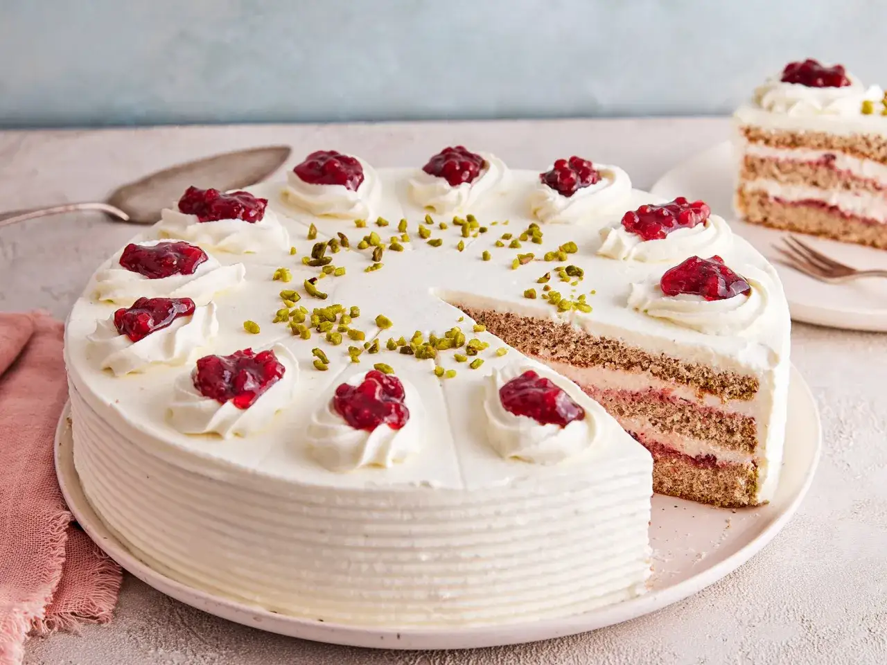 Ein saftiger buchweizen kuchen mit Sahne, roten Beeren und Pistazien. Ein St&uuml;ck ist bereits angeschnitten.