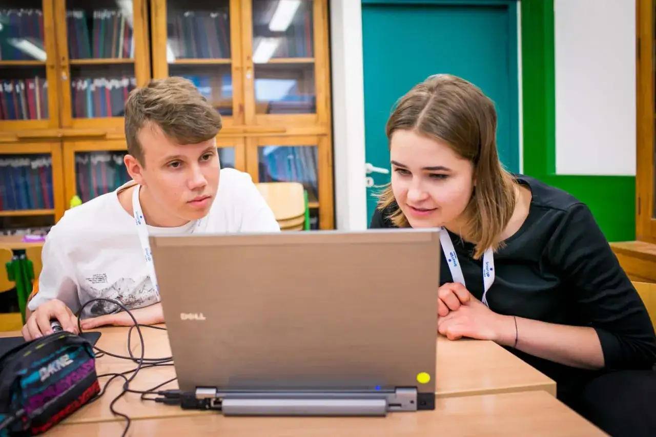 Dwóch uczniów pracuje przy laptopie, ucząc się w ramach liceum online dla młodzieży.