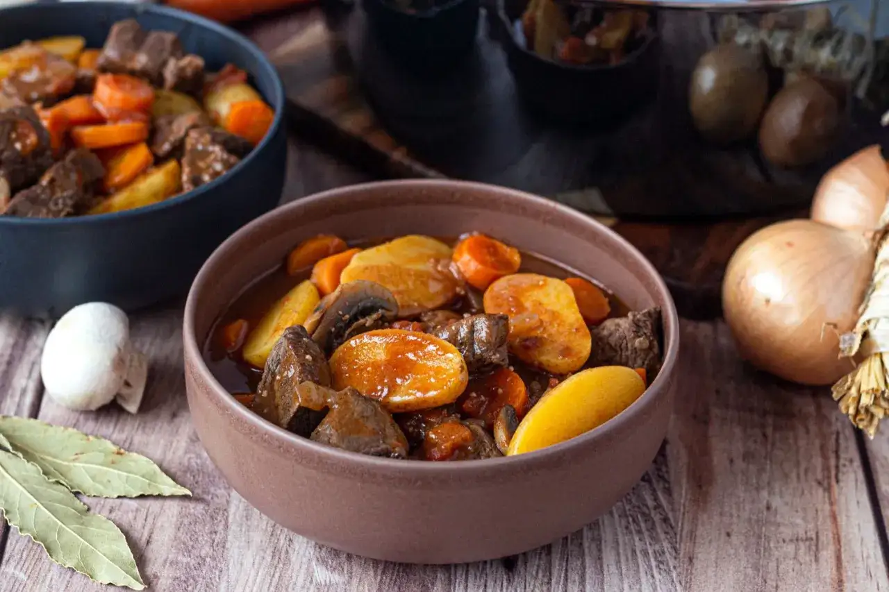 Un réconfortant plat de recette de boeuf mijoté, avec des morceaux de viande tendre, des carottes, des pommes de terre et des champignons, servi dans un bol.