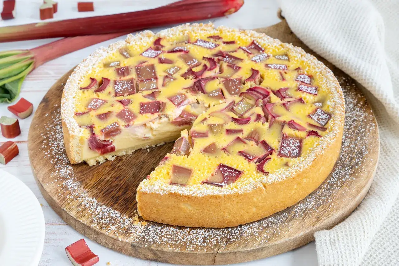 Ein saftiger Rhabarberkuchen mit Schmand, bestreut mit Puderzucker. Frische Rhabarberst&uuml;cke auf einem cremigen Boden.