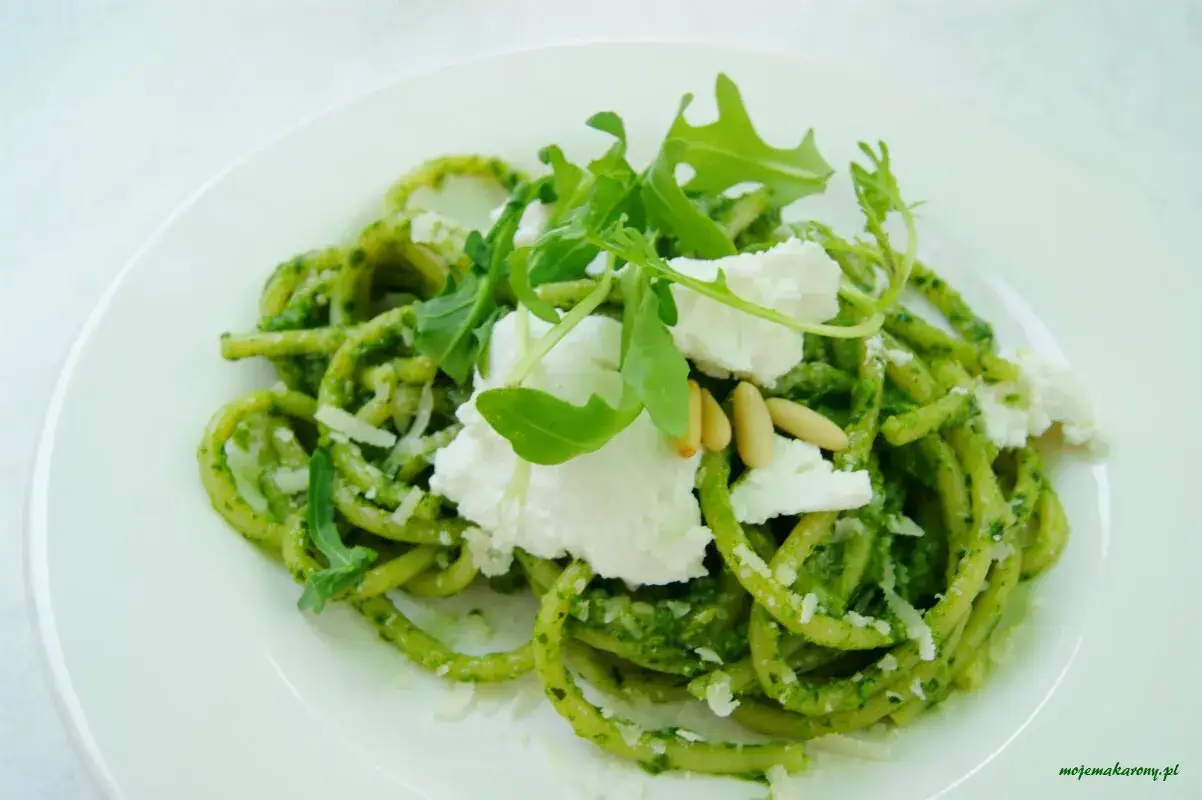 Zielony makaron z pesto, udekorowany serkiem ricotta, rukolą i orzeszkami pinii. Pyszne danie, które zachwyca smakiem.