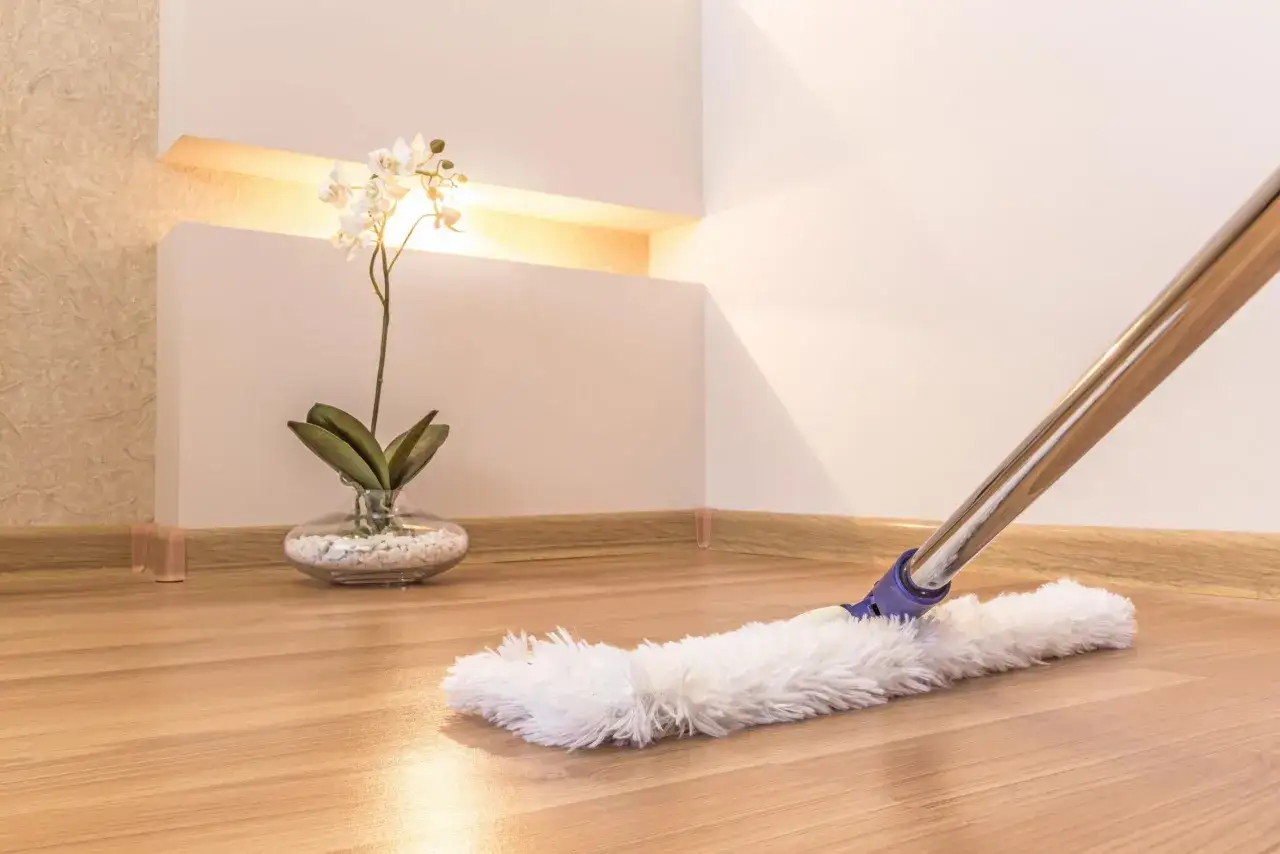Un plumero blanco se desliza sobre un suelo de madera, listo para limpiar parquet. Una orqu&iacute;dea blanca decora el rinc&oacute;n.