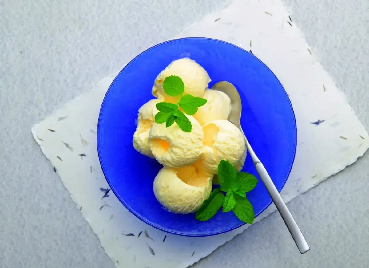 Kremowe, domowe lody śmietankowe w niebieskiej miseczce, ozdobione listkami mięty. Idealne na gorące dni.