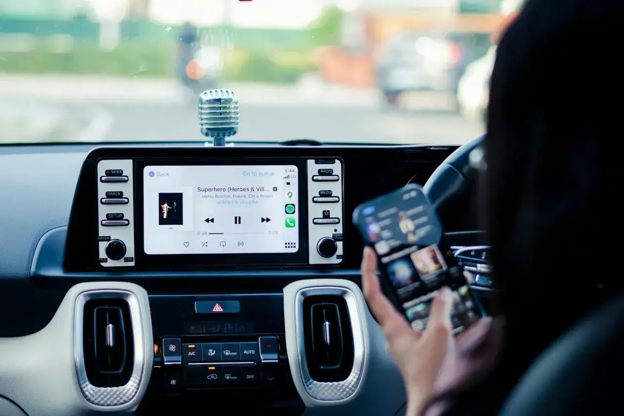 Wnętrze samochodu Skoda z ekranem multimedialnym wyświetlającym utwór muzyczny i smartfonem w dłoni, gotowym do połączenia przez Skoda Connect.