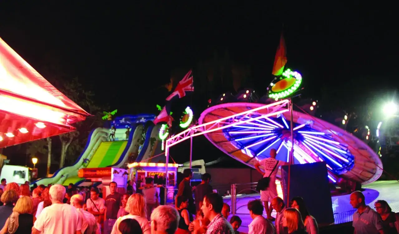 Ambiance de f&ecirc;te foraine 84, attractions lumineuses, toboggan gonflable et foule anim&eacute;e sous le ciel nocturne.