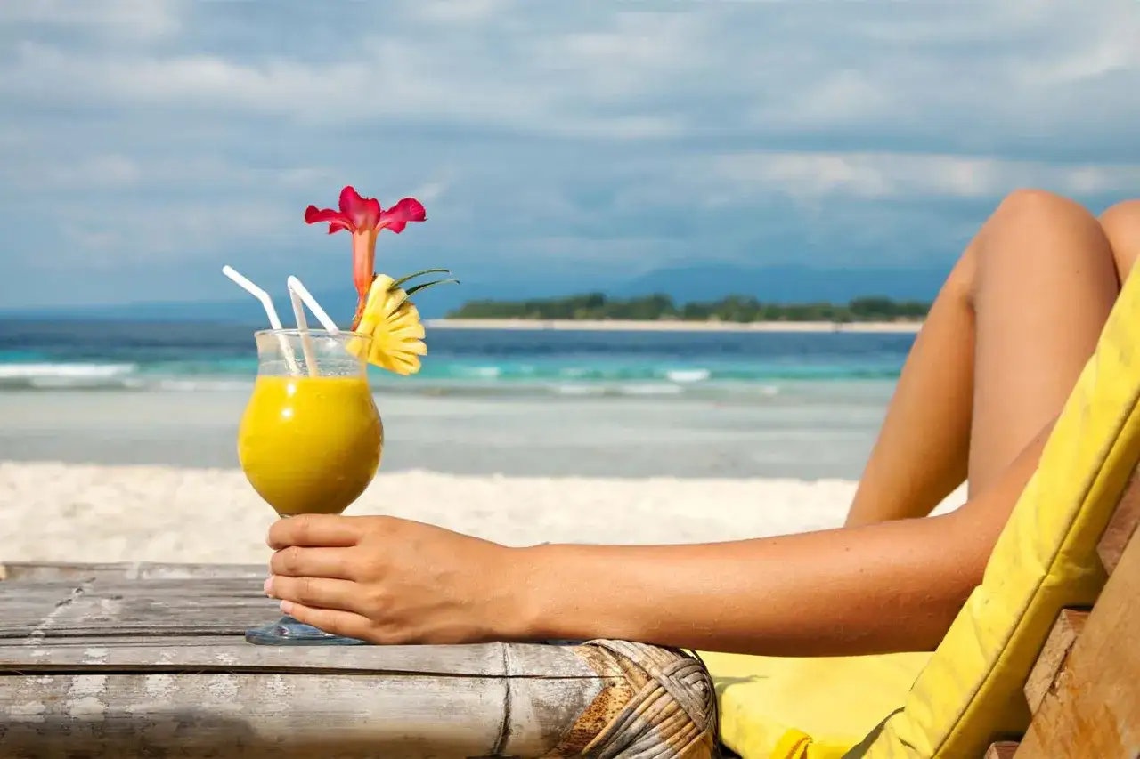 Orzeźwiający drink z palemką, ozdobiony ananasem i kwiatem, na tle rajskiej plaży. Idealny na wakacyjny relaks.