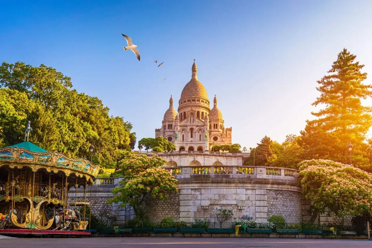 Bajkowy karuzela i bazylika Sacré-Cœur na Montmartre w Paryżu, z mewą szybującą na tle błękitnego nieba.