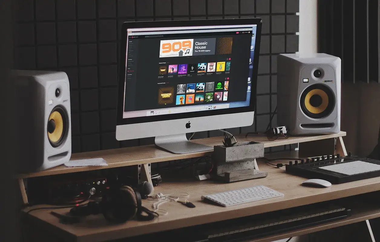Ein Musikproduktions-Setup mit Studio-Monitoren, iMac, Tastatur und Kopfhörern. Ein klassisches Beispiel für Gear Acquisition Syndrome, das die Leidenschaft für neue Ausrüstung zeigt.