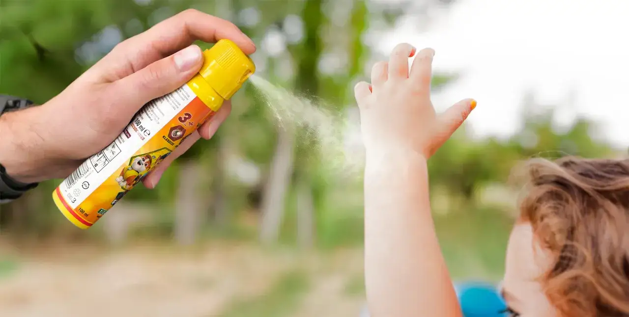 Ochrona przed ugryzieniem komara u dziecka. Ręka dorosłego aplikuje spray na rękę malucha.