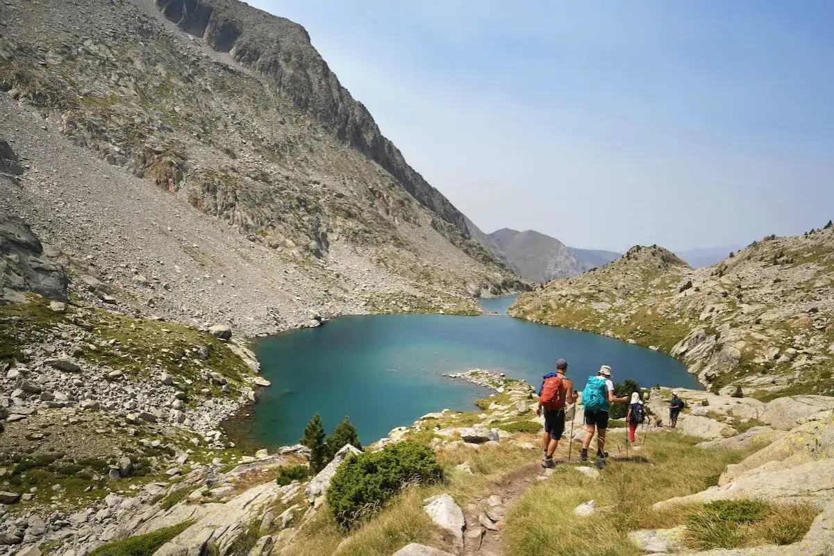Senderistas disfrutan de las impresionantes rutas de Benasque, con un lago turquesa rodeado de montañas rocosas.