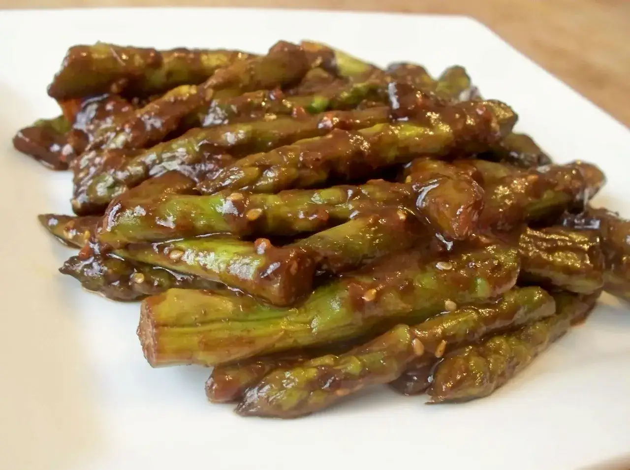 Ein Haufen glasiertes **spargel asiatisch** mit Sesam auf einem wei&szlig;en Teller.