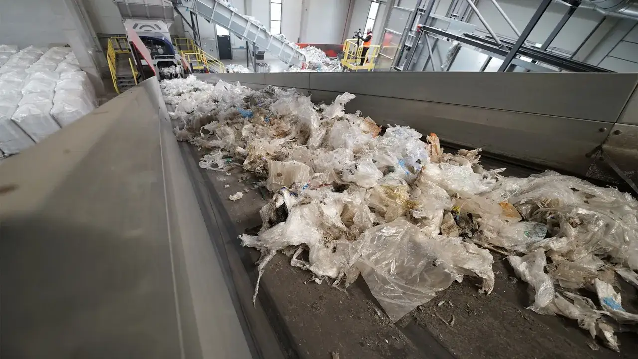 Stos białych work&oacute;w czeka na recykling folii. Taśmociąg transportuje zużyte opakowania do przetworzenia.