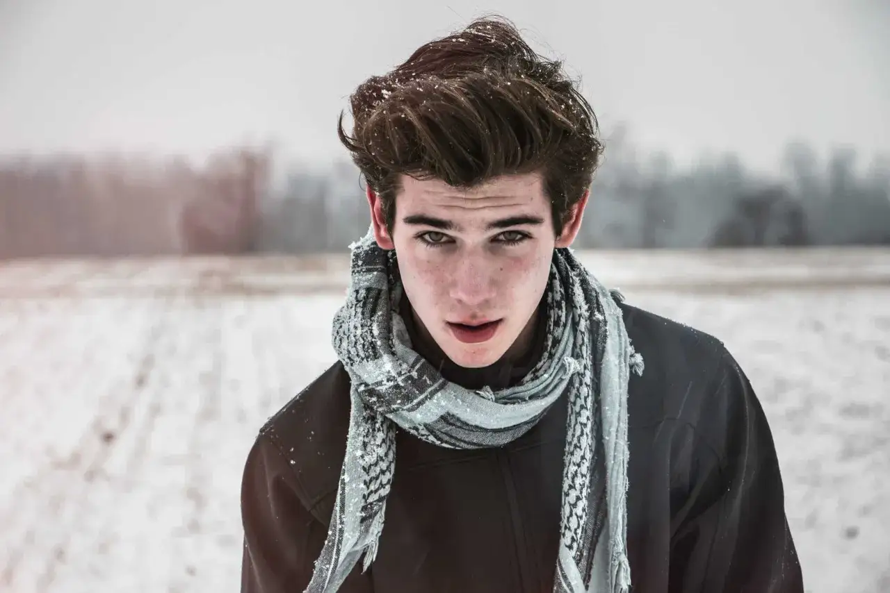 Un jeune homme au nez rouge froid, les cheveux mouill&eacute;s par la neige, regarde intens&eacute;ment, envelopp&eacute; dans une &eacute;charpe.