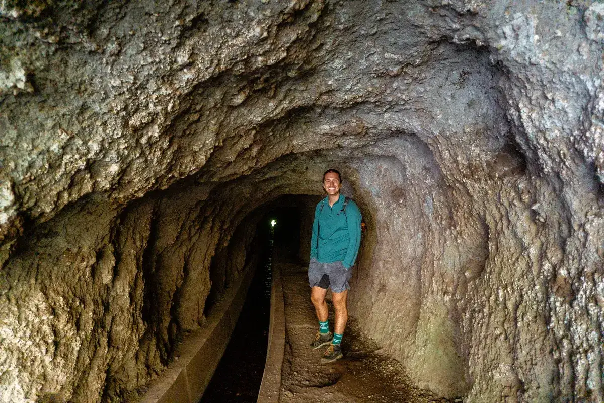 Un randonneur sourit dans un tunnel de levada à Madère, un canal d'eau coule à sa gauche.