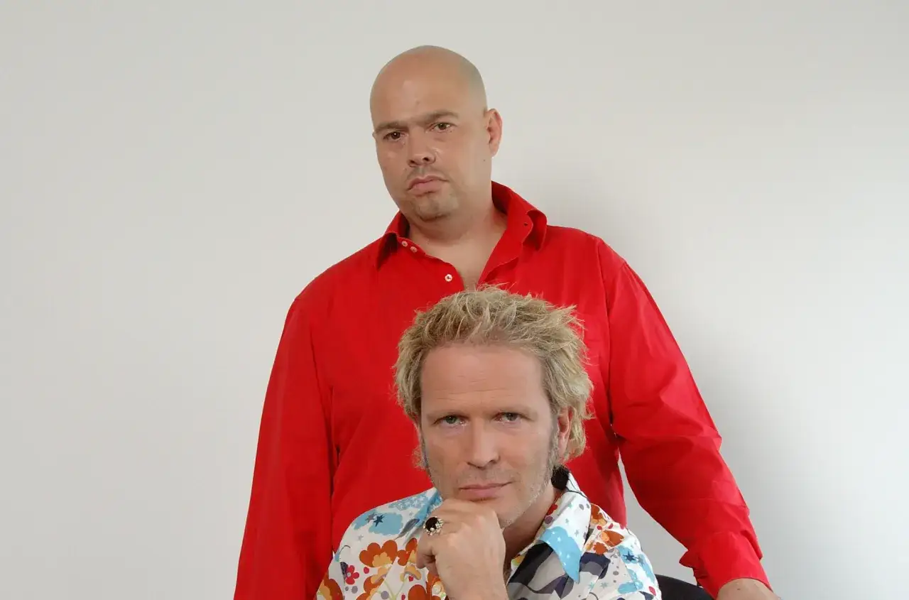 Zwei Männer, einer mit Glatze und rotem Hemd, der andere mit blonden Haaren und buntem Hemd, posieren für ein Foto. Sie sind jam el mar.