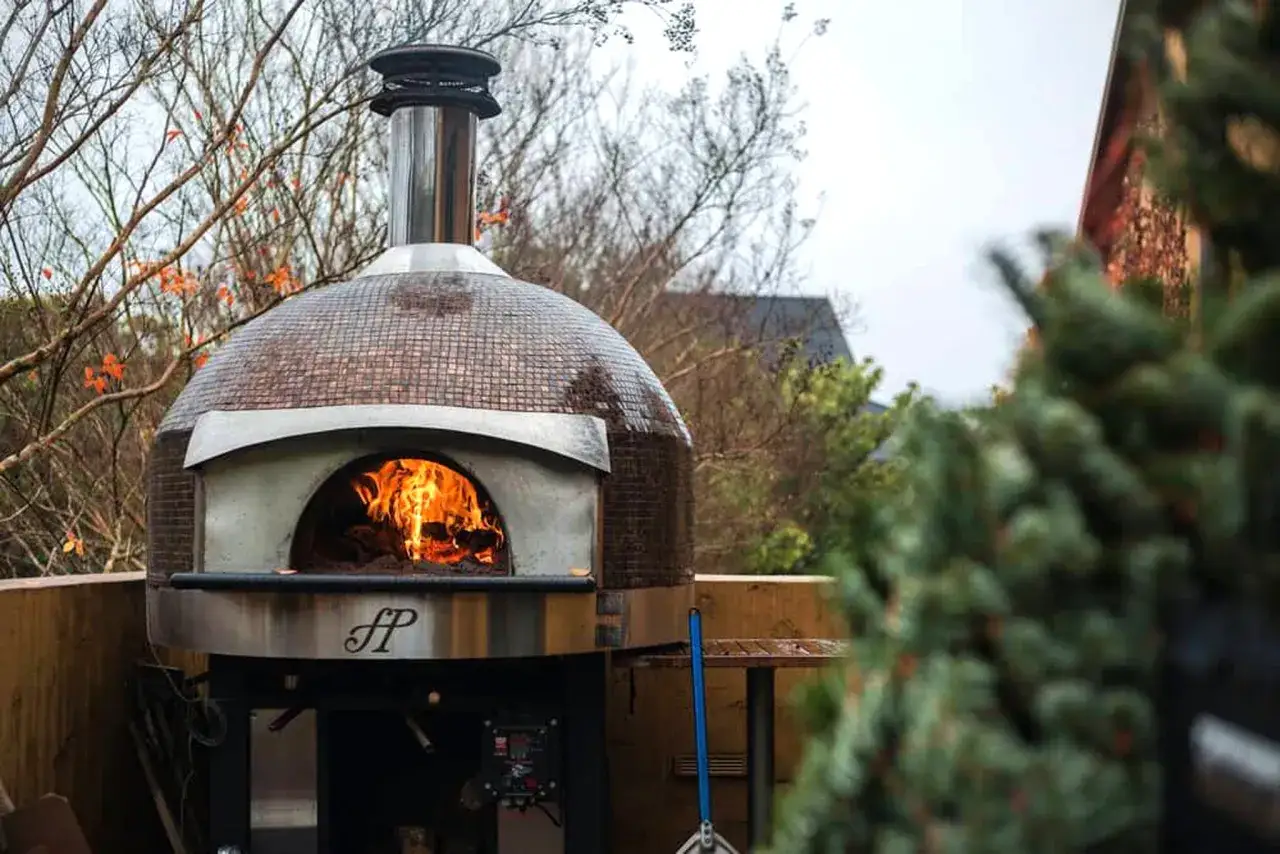En vackert **byggd pizzaugn** med glödande eld i öppningen, redo för att baka perfekta pizzor utomhus.