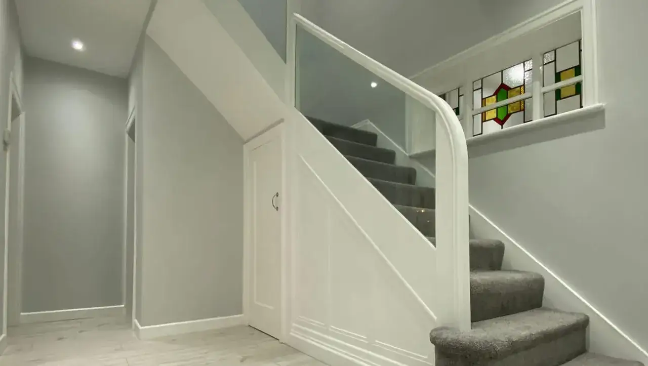 Peinture d'un couloir et de portes, avec un escalier moderne et un vitrail coloré.