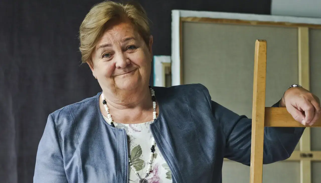 Uśmiechnięta Aleksandra Piotrowska, psycholog, opiera się o drewniane krzesło. Jej wiek jest trudny do określenia, ale emanuje ciepłem.