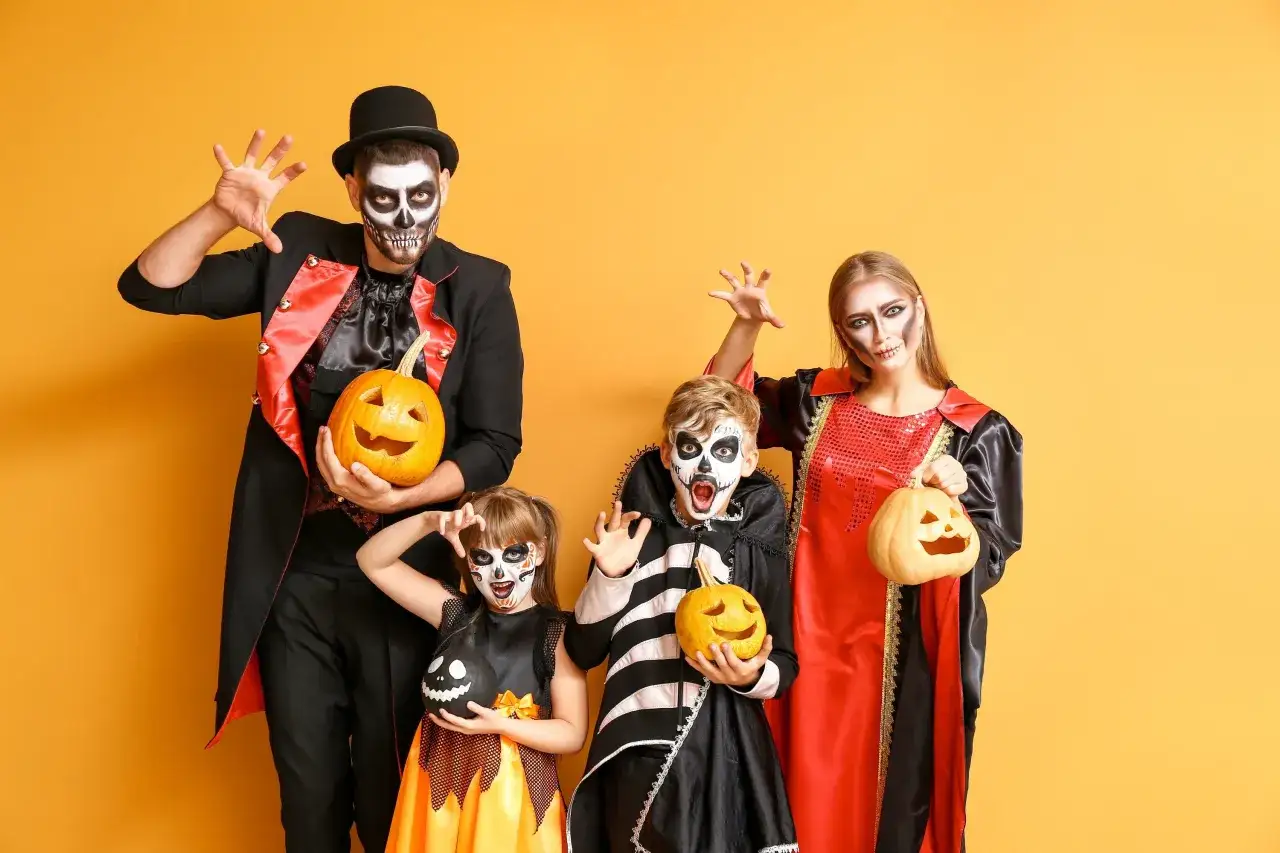 Rodzina w strojach szkieletów i wampirów, z dyniami, pokazuje, jak zrobić przebranie na Halloween.