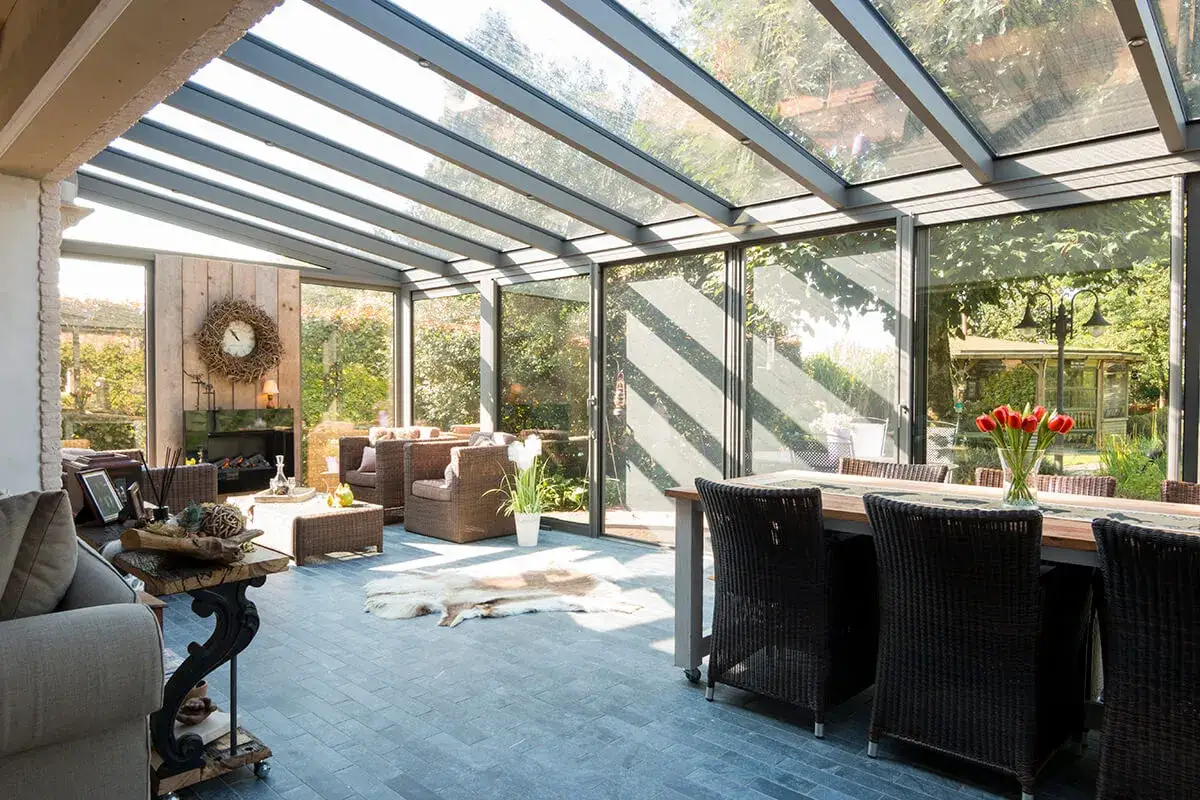Aménagement véranda lumineux avec salon confortable, cheminée et salle à manger. Vue sur jardin verdoyant.