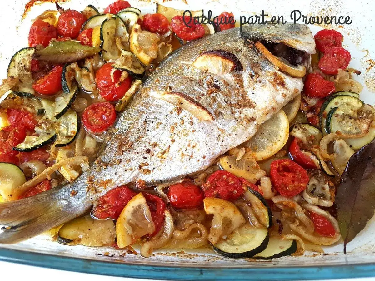 Un filet de daurade r&ocirc;ti avec tomates cerises, courgettes, citrons et oignons dans un plat en verre.