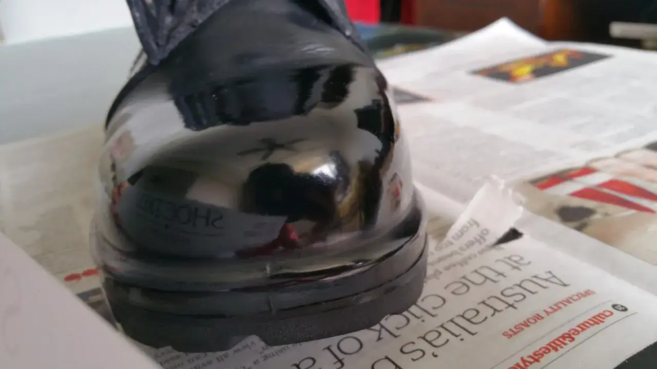 Glänzender schwarzer Schuh, der auf Zeitungspapier steht. Perfekt, um zu zeigen, wie man Lackschuhe pflegen kann.