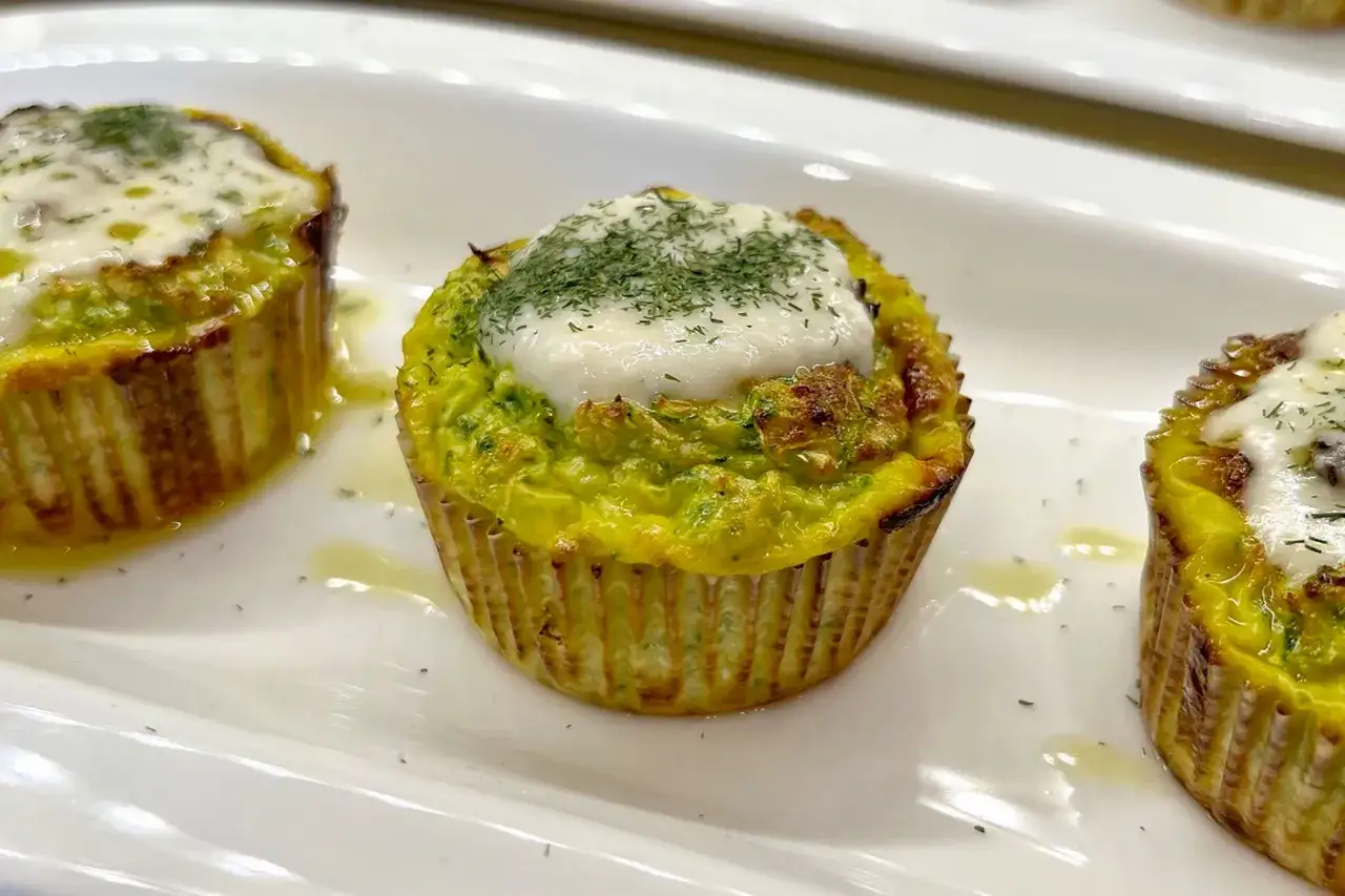 Tre tortini di zucchine dorati, guarniti con formaggio fuso e erbe aromatiche, serviti su un piatto bianco.