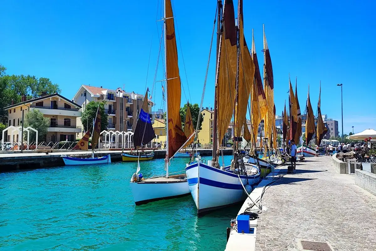 Vele spiegate nel porto di Igea Marina, centro storico. Barche tradizionali ormeggiate in un mare cristallino sotto un cielo azzurro.