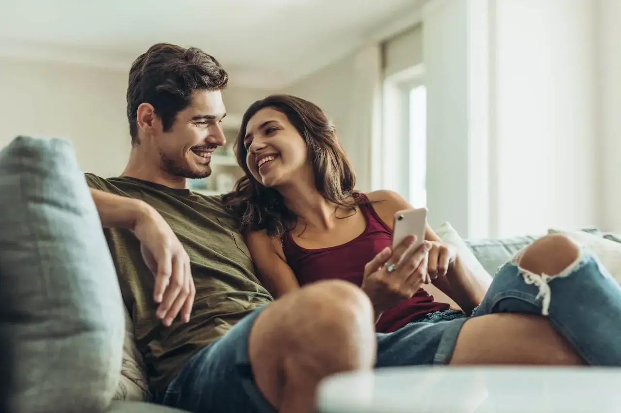 Pareja sonriente en el sof&aacute;, compartiendo un momento &iacute;ntimo. Un ejemplo de comunicaci&oacute;n efectiva, donde la conexi&oacute;n visual y la cercan&iacute;a transmiten afecto.