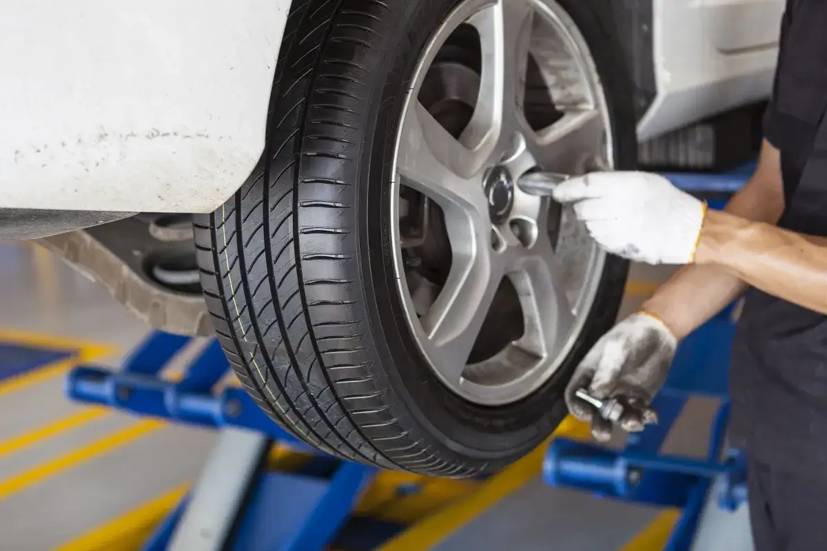Mecánico con guantes blancos usa una llave para arreglar neumático pinchado de un coche elevado en un taller.
