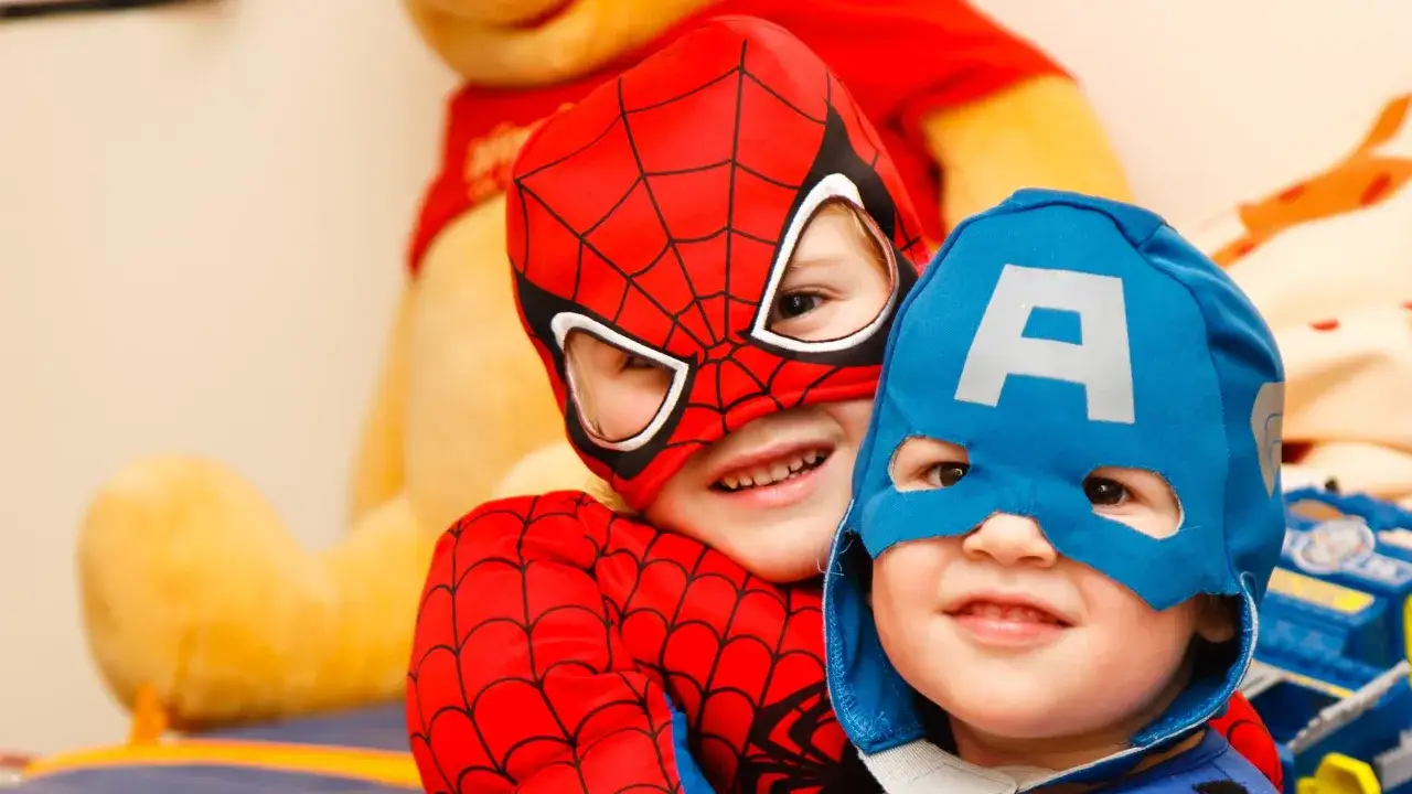 Dwóch chłopców w strojach superbohaterów, Spider-Mana i Kapitana Ameryki, uśmiecha się do aparatu. To świetny sposób, by pokazać, jak nauczyć dziecko angielskiego przez zabawę.