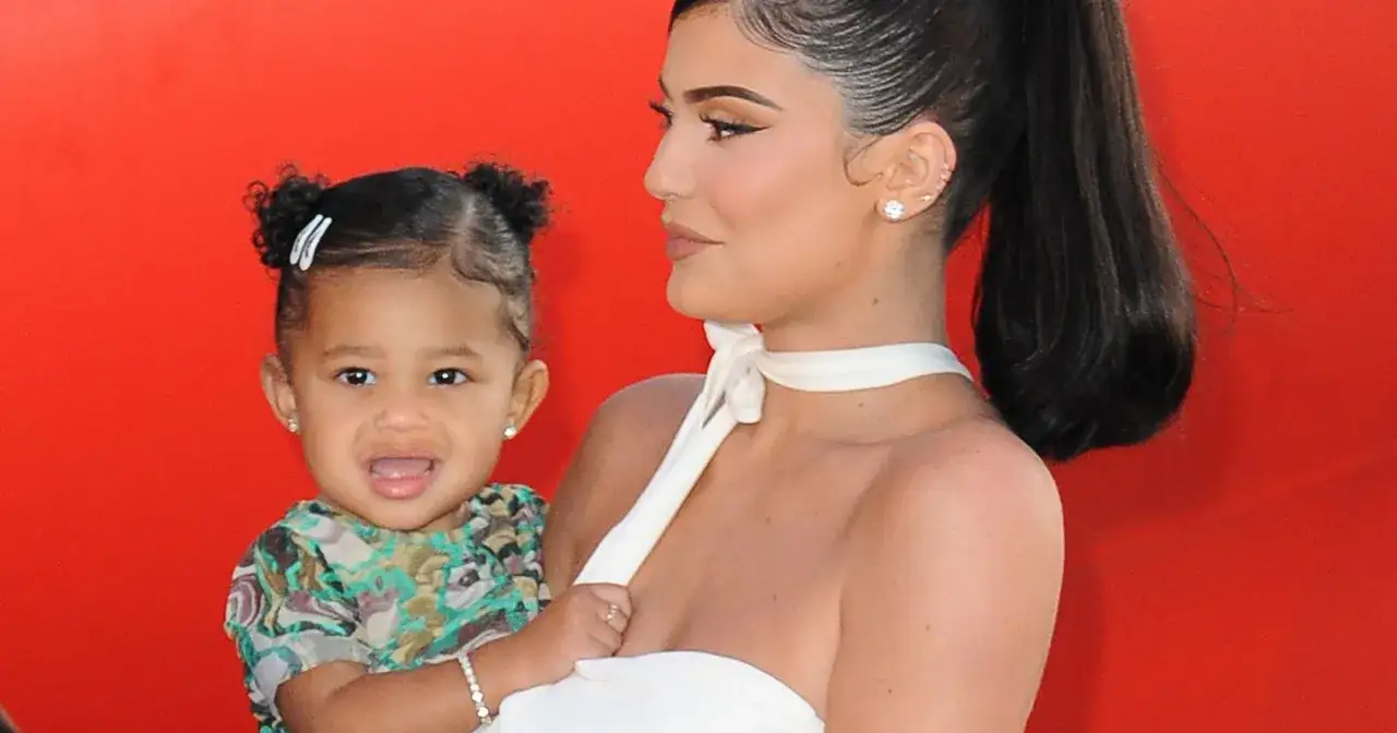Kylie Jenner trzyma swoje urocze dziecko, które ma na sobie kolorową bluzkę i błyszczące kolczyki.