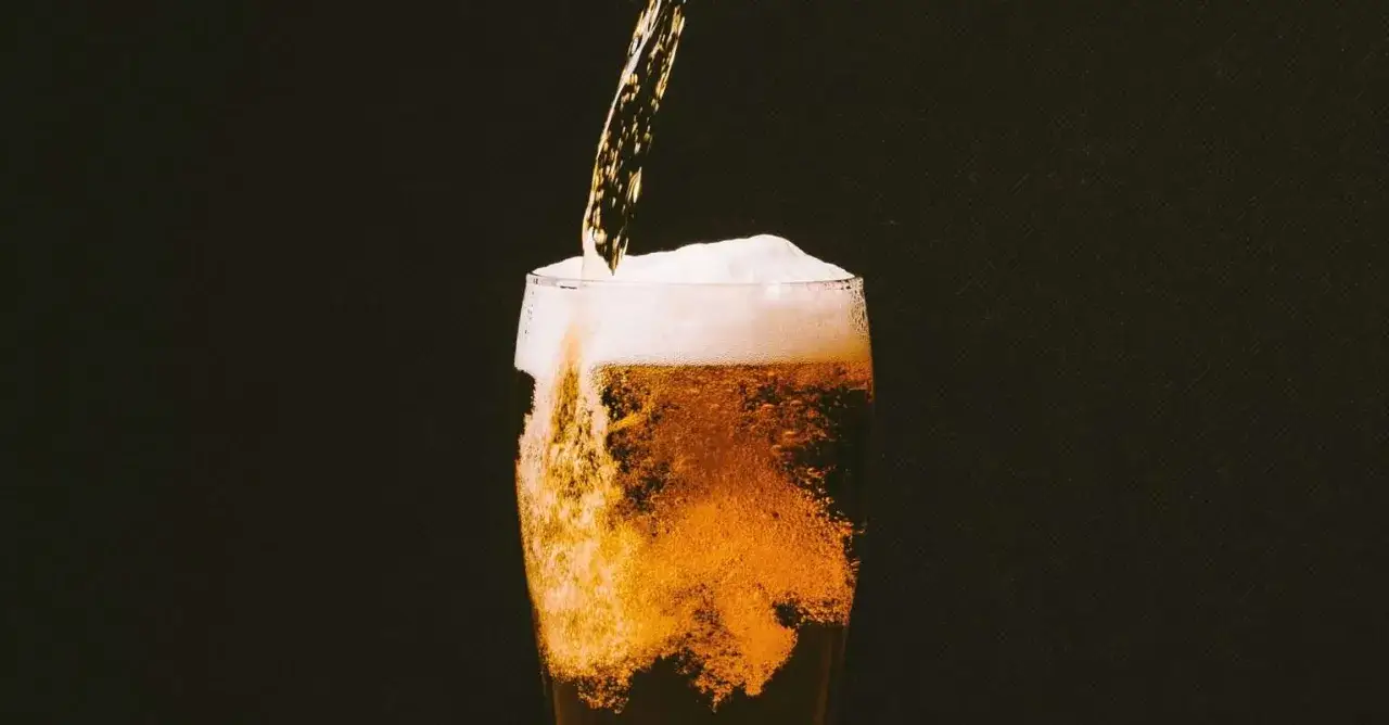 Birra versata in un bicchiere, creando una schiuma abbondante. Attenzione, la schiuma della birra fa male se consumata in eccesso.