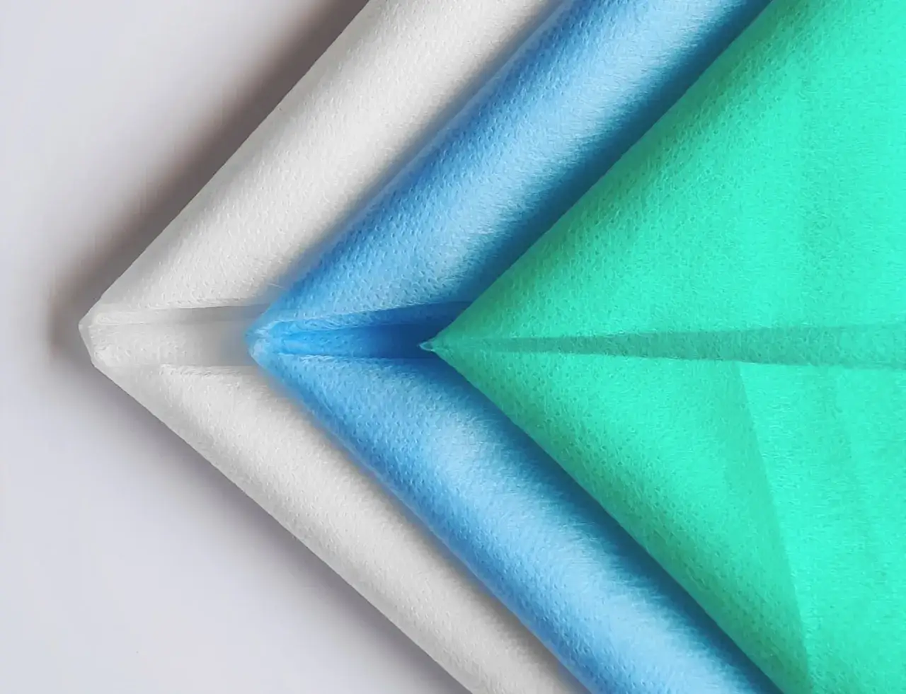 Warstwy białego, niebieskiego i zielonego materiału **non woven** ułożone w kształt wachlarza.