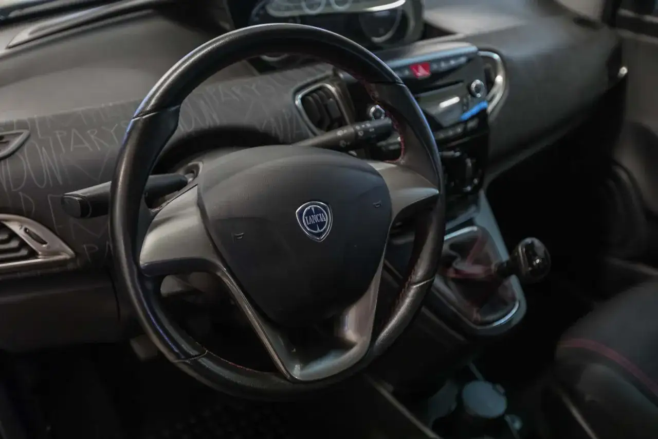 Volante e cambio di una Lancia Ypsilon 1.3 Multijet Diesel. Interni eleganti con cuciture rosse a contrasto.