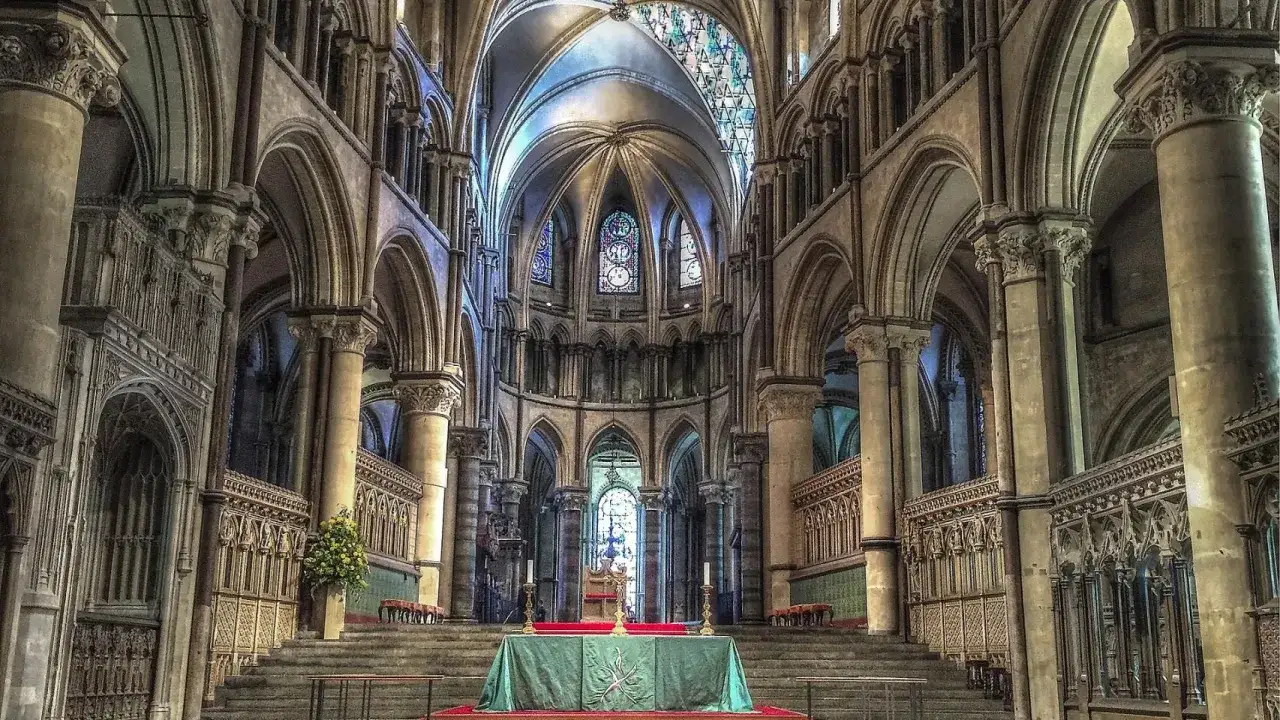 Interior de una majestuosa catedral gótica, con arcos elevados, bóvedas intrincadas y vitrales que iluminan el espacio.