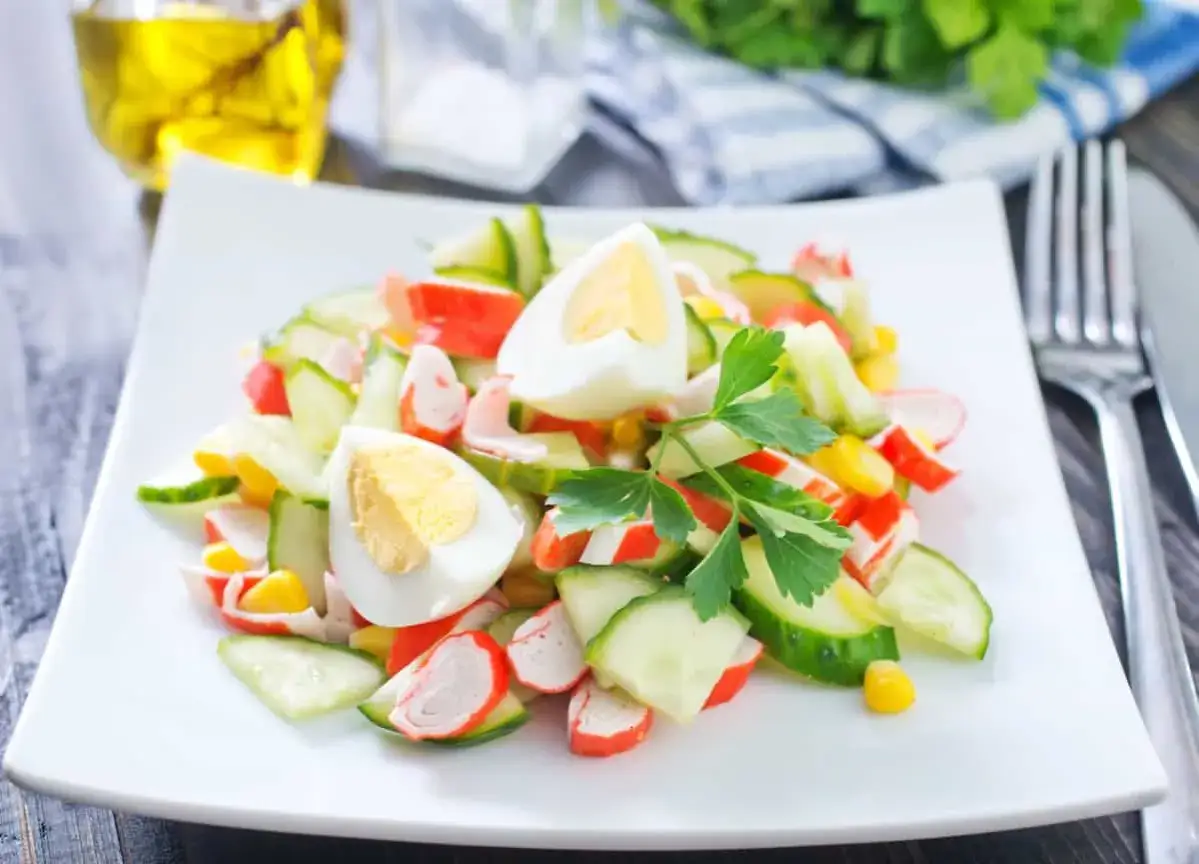 Deliciosa ensalada de cangrejo con pepino, huevo duro y ma&iacute;z, adornada con perejil fresco.