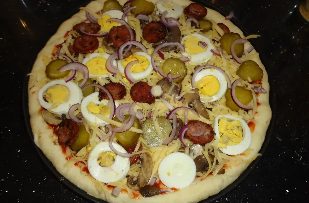 Gotowa do pieczenia pizza farmerska z jajkiem, kiełbasą, ogórkiem i cebulą.