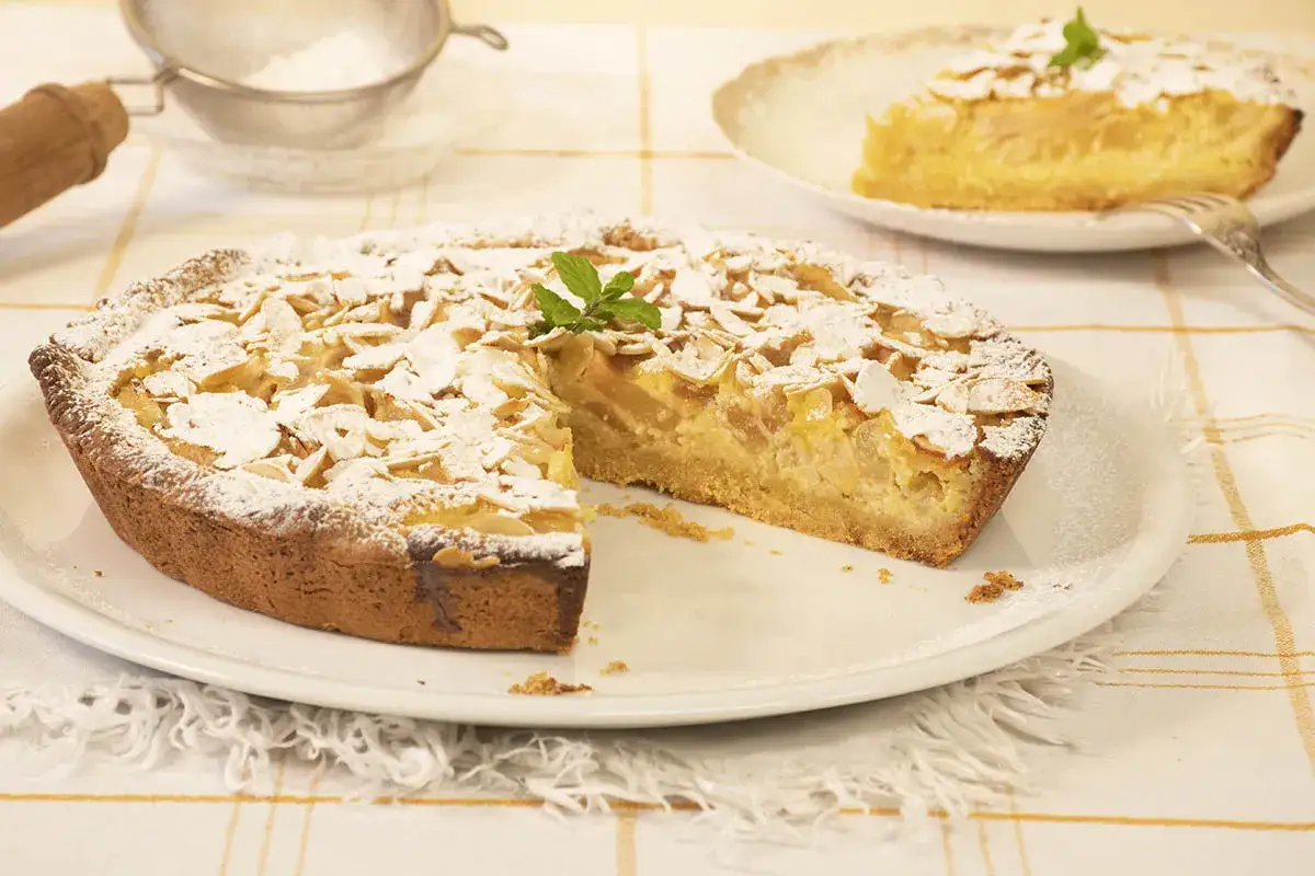 Deliciosa tarta de pera, cubierta de almendras laminadas y espolvoreada con azúcar glas. Una rebanada ya servida.