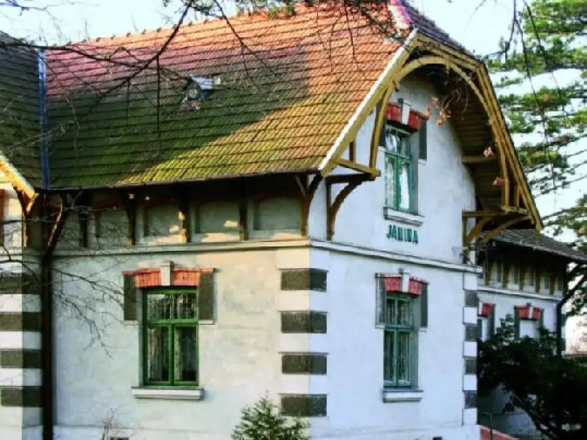 Stary dom z zielonymi oknami i dachówkami, objęty ochroną konserwatorską, nosi napis 