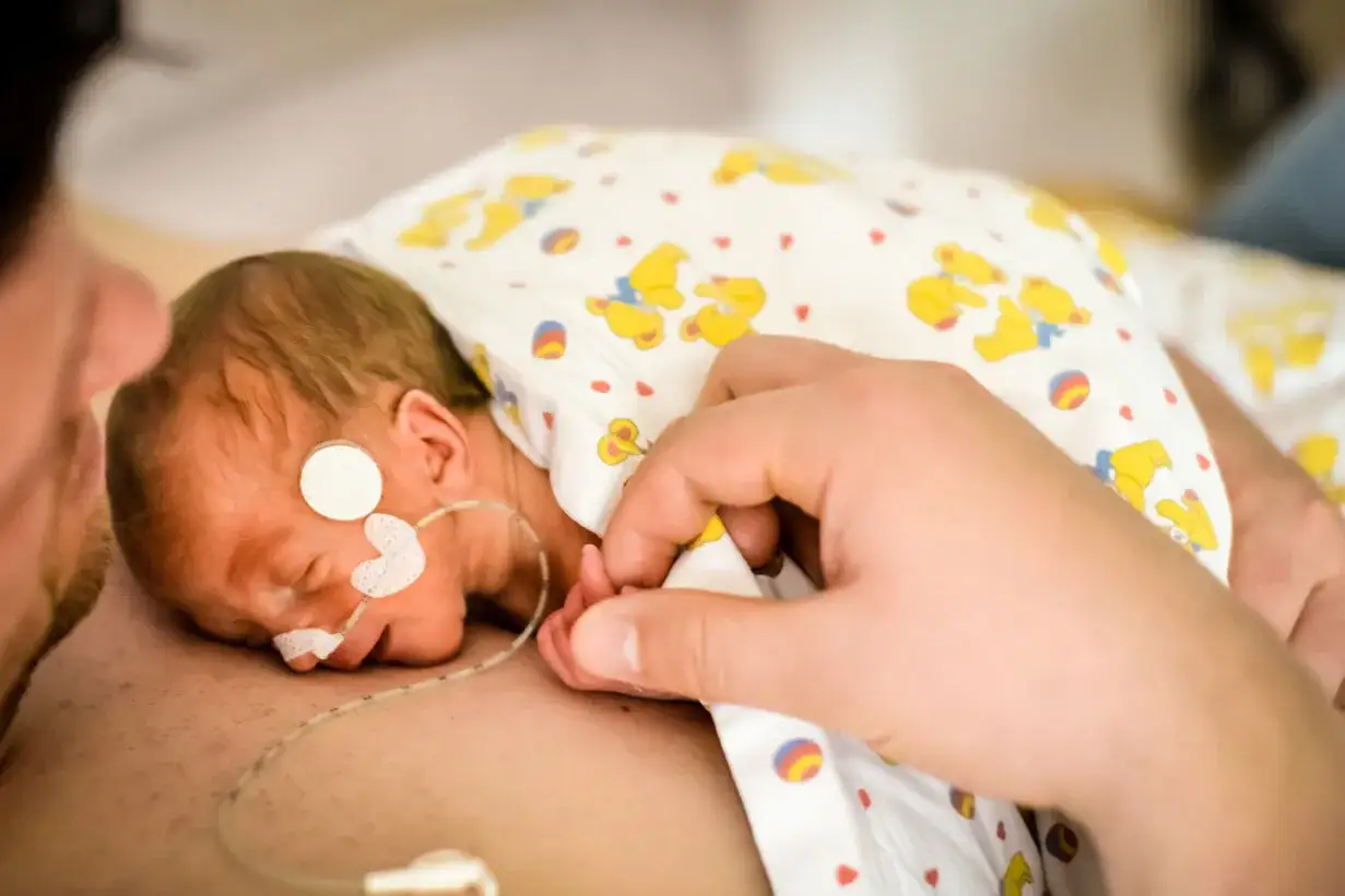 Malutki wcześniak, otulony kocykiem z misiami, śpi na klatce piersiowej taty. Delikatny dotyk dłoni.