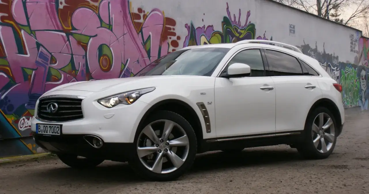 Biały infiniti samochód zaparkowany przed ścianą z kolorowym graffiti.