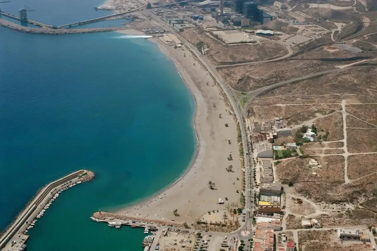 Vista aérea de la playa de las Martinicas, con su arena dorada, el mar turquesa y un puerto deportivo lleno de barcos.