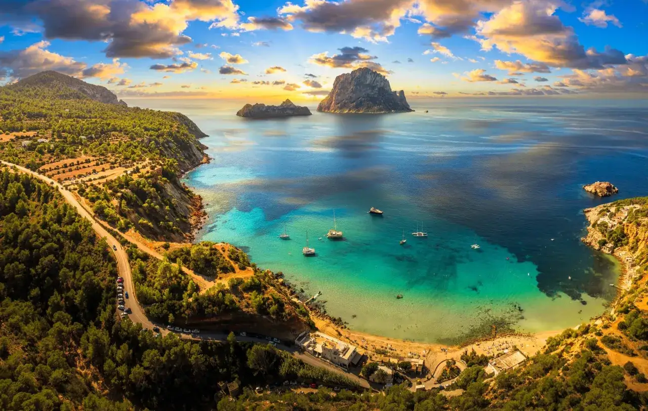 Zachód słońca nad Ibizą, idealna ibiza pogoda. Turkusowa woda, łodzie i skaliste wysepki Es Vedrà.
