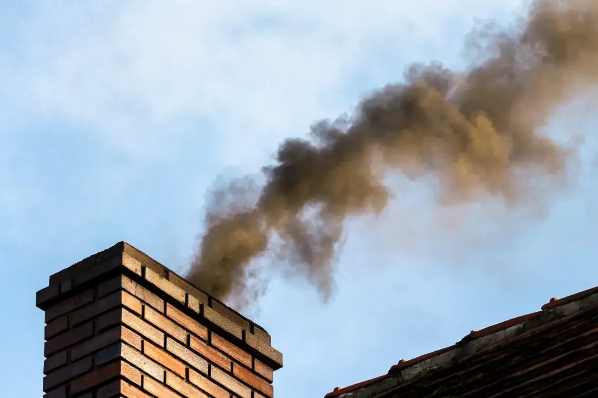 Fum&eacute;e noire s'&eacute;chappant d'une chemin&eacute;e en briques, signe d'un incendie ou d'une combustion intense.