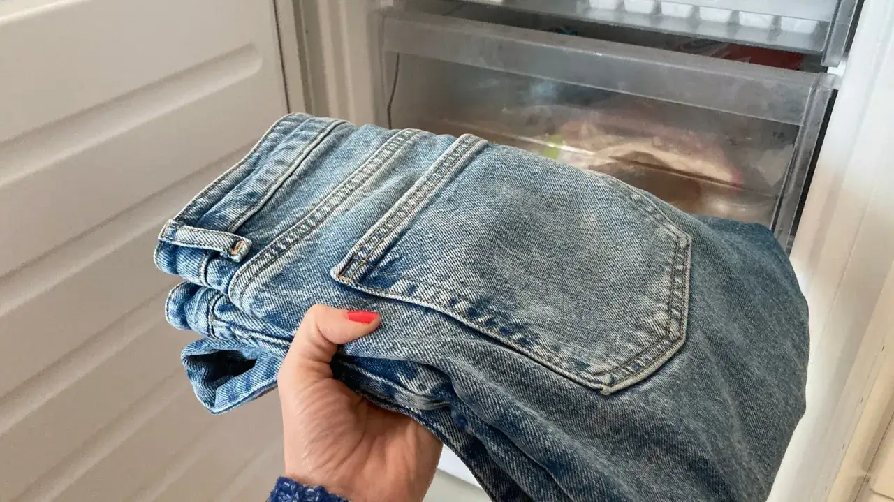 En hand h&aring;ller ett par vikta jeans framf&ouml;r en &ouml;ppen frys. Kanske f&ouml;r att fr&auml;scha upp jeansen?